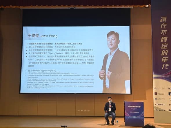 年會講台上的講者與投影幕，投影片為王俊傑 Jawin Wang 的講者介紹