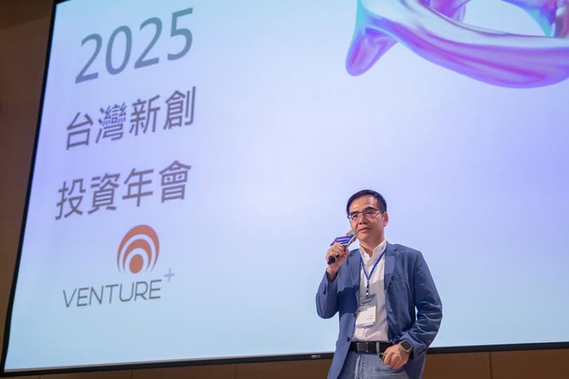 講者站在「2025 台灣新創投資年會」與 VENTURE+ 標誌的投影幕前演講